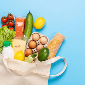 Shopping bag full of healthy food on blue background. Flat lay with copy space